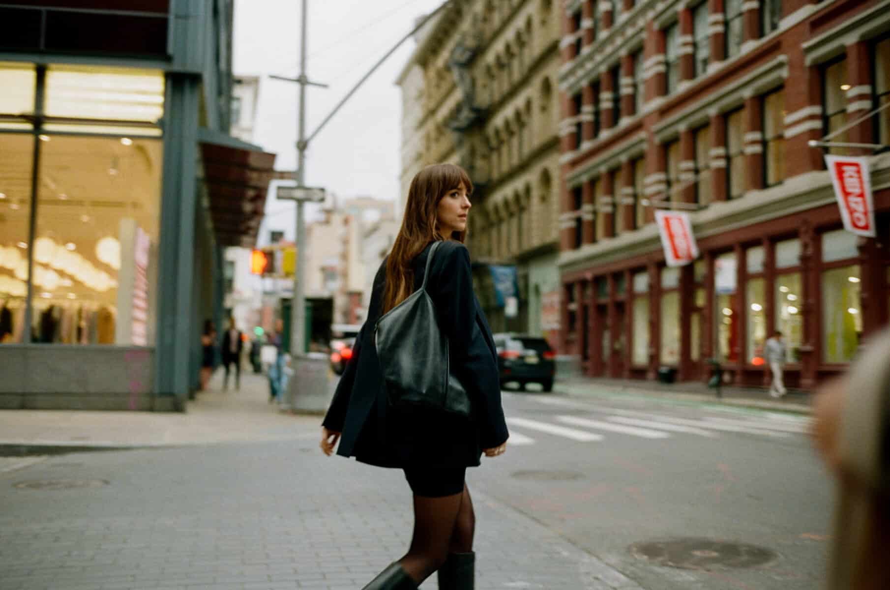 City street scene featuring a woman with a black handbag and stylish outfit for fashion blogging. Dakota Johnson in Materialists (2024). Photo by Atsushi Nishijima. © A24. Image courtesy of A24 Press.