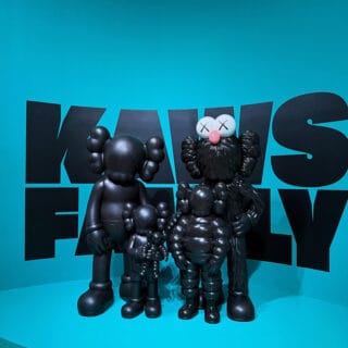 Colorful Kaws figurines at modern art exhibit with blue background.