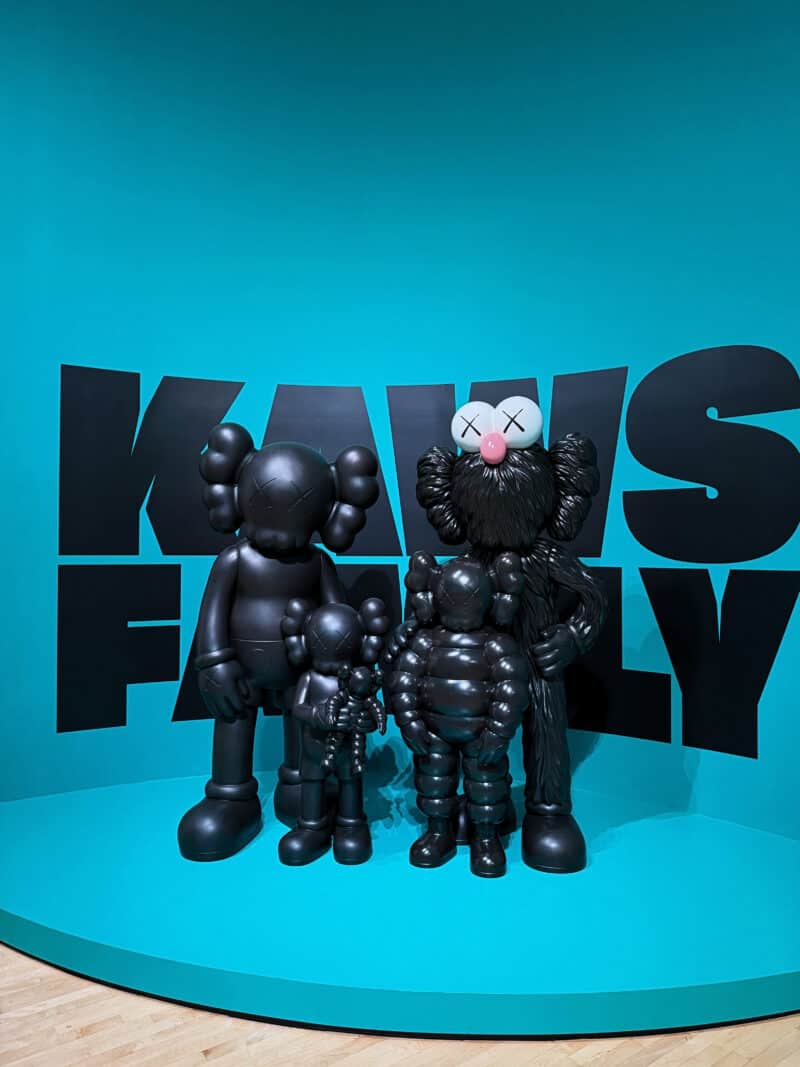 Colorful Kaws figurines at modern art exhibit with blue background.